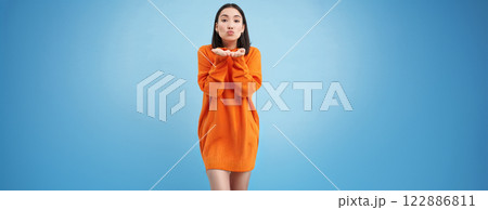 Beautiful korean girl puckers lips, blows air kiss at camera, stands cute against blue background Beautiful korean girl puckers lips, blows air kiss at camera, stands cute against blue background 122886811