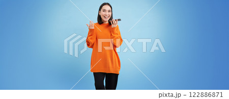 Cheerful smiling korean woman talk on speakerphone, records voice message, learns how to speak using language learning mobile app, blue background 122886871