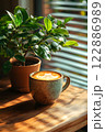 Morning coffee with latte art on a wooden table next to a potted plant. Perfect for promoting a cafe or creating a relaxing atmosphere on social media. It gives a feeling of warmth start to the day. 122886989