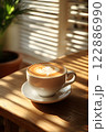 Morning coffee with latte art on a wooden table next to a potted plant. Perfect for promoting a cafe or creating a relaxing atmosphere on social media. It gives a feeling of warmth start to the day. 122886990