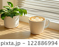 Morning coffee with latte art on a wooden table next to a potted plant. Perfect for promoting a cafe or creating a relaxing atmosphere on social media. It gives a feeling of warmth start to the day. 122886994