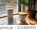 Morning coffee with latte art on a wooden table next to a potted plant. Perfect for promoting a cafe or creating a relaxing atmosphere on social media. It gives a feeling of warmth start to the day. 122886995