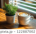 Morning coffee with latte art on a wooden table next to a potted plant. Perfect for promoting a cafe or creating a relaxing atmosphere on social media. It gives a feeling of warmth start to the day. 122887002