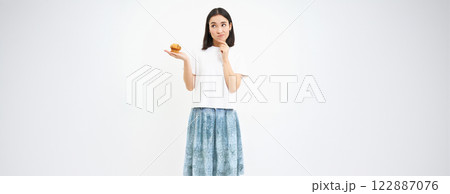 Woman with pensive face, holding cupcake and thinking, white background 122887076