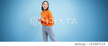 Portrait of young Chinese woman, teacher or student with digital tablet and pencil, writing, taking notes, doing her homework, standing over blue background Portrait of young Chinese woman, teacher or student with digital tablet and pencil, writing, taking notes, doing her homework, standing over blue background 122887124