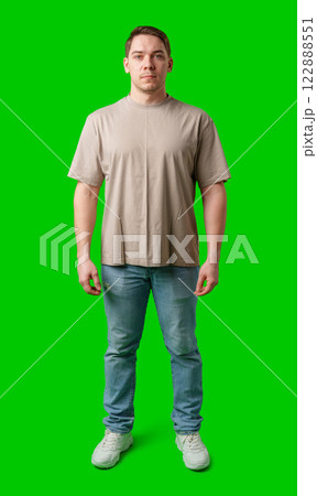 Young man stands confidently in a plain beige t-shirt and jeans against a bright green background Young man stands confidently in a plain beige t-shirt and jeans against a bright green background 122888551