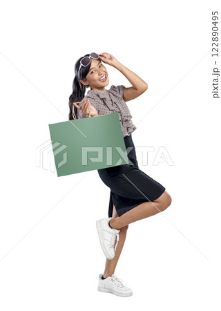 Portrait of an Asian Indonesian woman with sunglasses carrying a shopping bag isolated over a white background. Copy space or mockup. Concept of shopping, lifestyle, or consumerism 122890495
