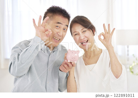 貯金箱を持つシニア夫婦 OKサイン リビング 貯金箱を持つシニア夫婦 OKサイン リビング 122891011