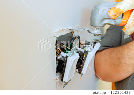 An electrician is repairing wall socket, using multi tools for electrical wires in residential environment. An electrician is repairing wall socket, using multi tools for electrical wires in residential environment. 122891428
