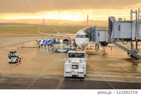 Airport baggage tug (baggage dolly transport) on duty and Ground Service fuel truck Refueling an aircraft at aircraft bay. 122892559