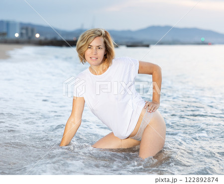 Lovely woman posing on sandy beach in sea waves Lovely woman posing on sandy beach in sea waves 122892874