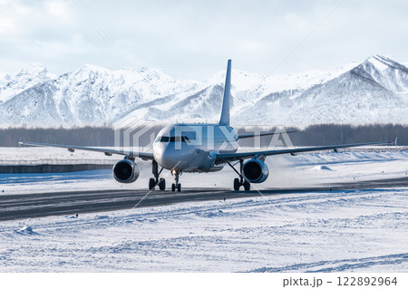 White passenger jet plane taxiing on taxiway in snowy winter day on the background of high snow capped mountains 122892964