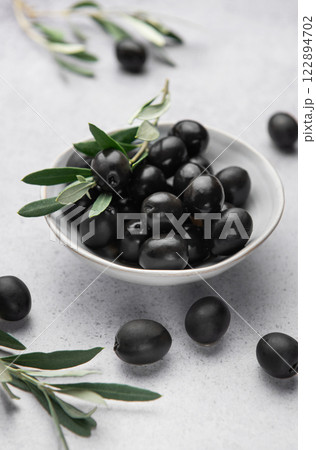 Black olives with olive branches served in ceramic bowl on gray background Black olives with olive branches served in ceramic bowl on gray background 122894702