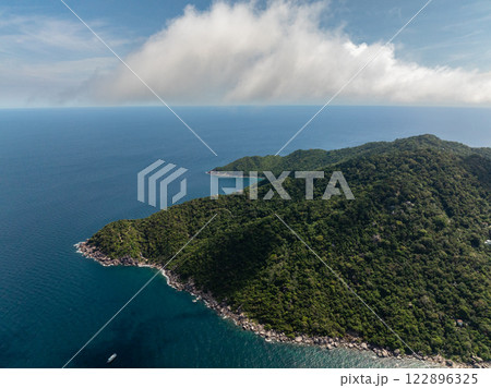 Lush green hills along the coastline meeting the deep blue sea under a partly cloudy sky. Ko Tao, Thailand. 122896325