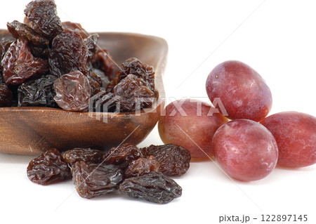 Dark raisins in wooden bowl next to bunch of red grapes, representing a healthy and delicious snack 122897145