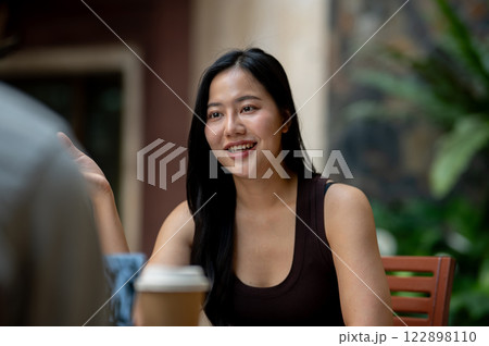 An attractive Asian woman enjoys a conversation with her friend during a meeting at a coffee shop. 122898110