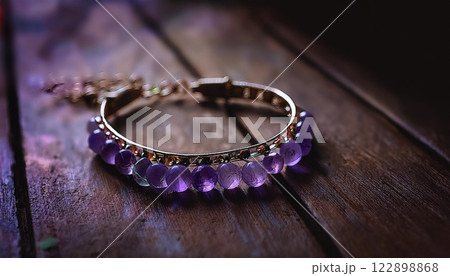 A purple bracelet with a gold clasp sits on a wooden surface 122898868