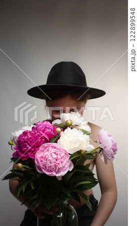 Elegant woman wearing a stylish hat adorned with peonies, captured in a vertical artistic portrait. Ideal for beauty, fashion, and floral-themed concepts Elegant woman wearing a stylish hat adorned with peonies, captured in a vertical artistic portrait. Ideal for beauty, fashion, and floral-themed concepts 122899548
