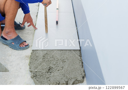 A detailed view of a worker leveling gray mortar with a tool, preparing for the placement of floor tiles in a house construction project. 122899567