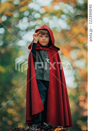 Cute cosplayer hobbit kid in cape costume in forest watching gold ring. Fantasy journey in fairytale Cute cosplayer hobbit kid in cape costume in forest watching gold ring. Fantasy journey in fairytale 122899840