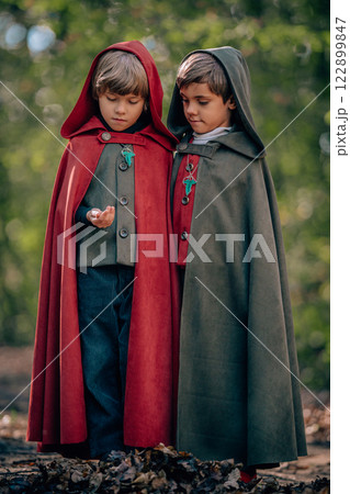 Hobbits boys in cape costumes standing in green forest with ring. Fantasy journey, halloween Hobbits boys in cape costumes standing in green forest with ring. Fantasy journey, halloween 122899847