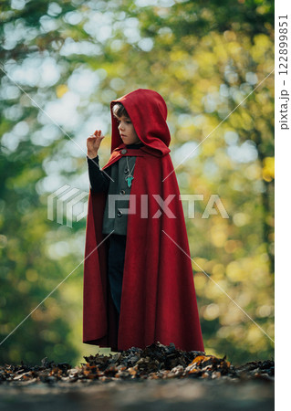 Cute cosplayer hobbit kid in cape costume in forest watching gold ring. Fantasy journey in fairytale Cute cosplayer hobbit kid in cape costume in forest watching gold ring. Fantasy journey in fairytale 122899851