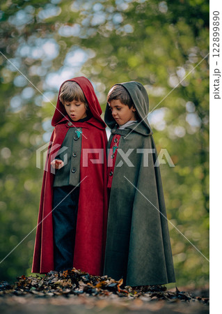 Hobbits boys in cape costumes standing in green forest with ring. Fantasy journey, halloween Hobbits boys in cape costumes standing in green forest with ring. Fantasy journey, halloween 122899890