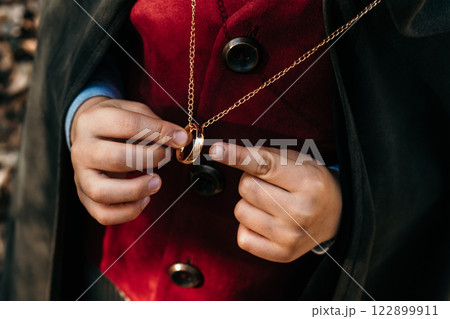 Unrecognizable child cosplayer in hobbit cape costume holding and wants to wear golden ring. Fantasy Unrecognizable child cosplayer in hobbit cape costume holding and wants to wear golden ring. Fantasy 122899911