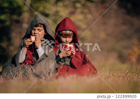 Hobbits boys in costumes sitting on autumn ground to eat apples. Fantasy journey, halloween 122899920