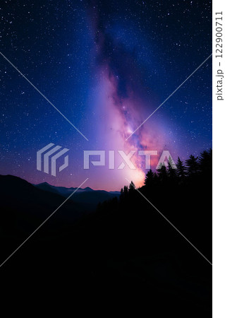 An image of a star-studded night sky with the bright Milky Way stretching over silhouettes of mountains and trees. Milky Way night landscape over forest and mountains. 122900711