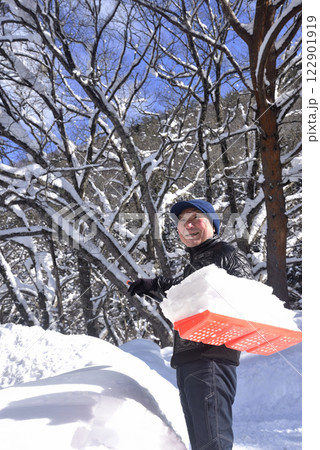 雪国で雪はねを使用して除雪をしている笑顔の老人 122901919