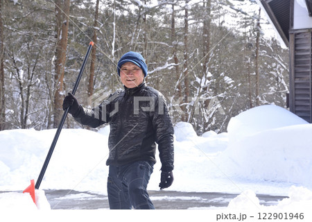 雪国で雪はねを使用して除雪をしている笑顔の老人 122901946