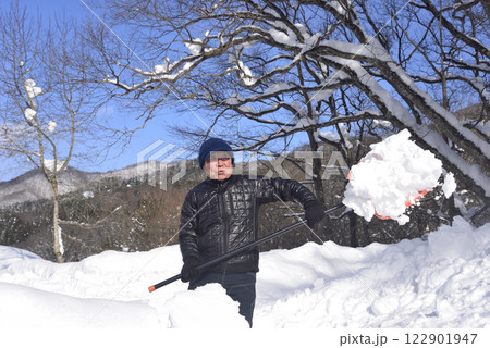 雪国で雪はねを使用して除雪をしている笑顔の老人 122901947