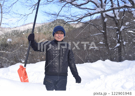雪国で雪はねを使用して除雪をしている笑顔の老人 122901948