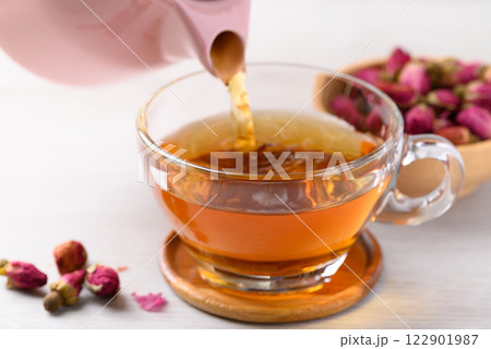 Rose bud tea in teapot pouring into cup glass on white background, Healthy flower tea 122901987