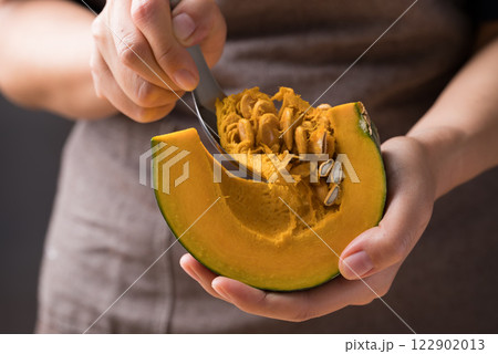 Hand holding spoon and removing seeds from pumpkin, Homemade cooking 122902013