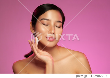 Glowing skin routine with a woman applying cream in a bright studio setting with pink background Glowing skin routine with a woman applying cream in a bright studio setting with pink background 122902207