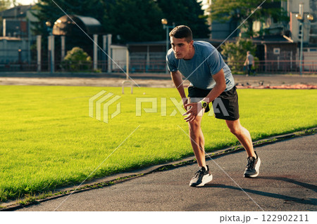 Man practicing sprinting on a track in an outdoor athletic facility during late afternoon Man practicing sprinting on a track in an outdoor athletic facility during late afternoon 122902211