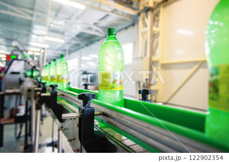Bottles of green liquid moving along a conveyor belt in a factory during daylight hours 122902354