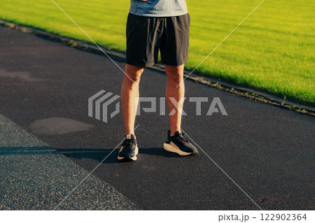 Athletic individual preparing for a workout on a sunny day at a park track with vibrant grass and black pavement Athletic individual preparing for a workout on a sunny day at a park track with vibrant grass and black pavement 122902364