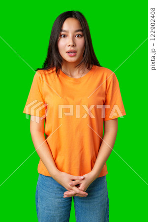 Young woman with long hair expressing surprise in an orange shirt against a green background 122902408