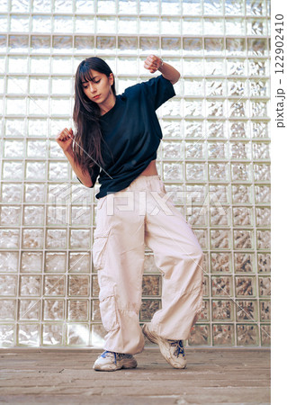 Young woman dances confidently in casual outfit in front of transparent glass wall during daytime 122902410