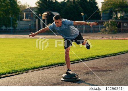 Man practicing balance on a stability board at an outdoor sports facility during daylight hours 122902414