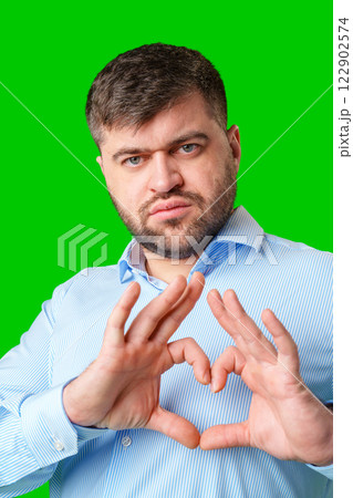 A man forming a heart shape with his hands against a vibrant green background 122902574