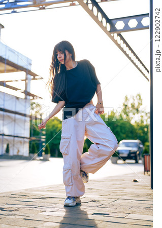 Young woman dancing outdoors in urban setting during golden hour with bright sunlight illuminating the surroundings Young woman dancing outdoors in urban setting during golden hour with bright sunlight illuminating the surroundings 122902742