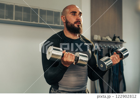 Fitness enthusiast performs strength training with dumbbells in a modern gym setting during daytime Fitness enthusiast performs strength training with dumbbells in a modern gym setting during daytime 122902812
