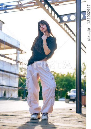 Young woman striking a pose outdoors in comfortable streetwear during golden hour in a modern urban setting 122902947