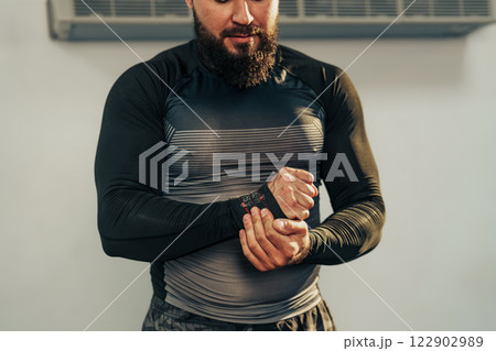 Man adjusts wrist support while preparing for workout in a gym setting with fitness equipment in the background 122902989