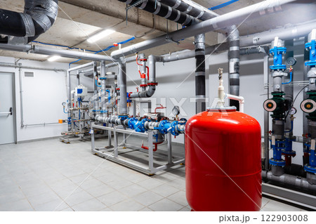 Equipment setup in a modern utility room featuring pipes, valves, and a large red tank Equipment setup in a modern utility room featuring pipes, valves, and a large red tank 122903008