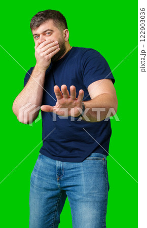 A man with a serious expression holds up both hands in a stopping gesture against a bright green background 122903036